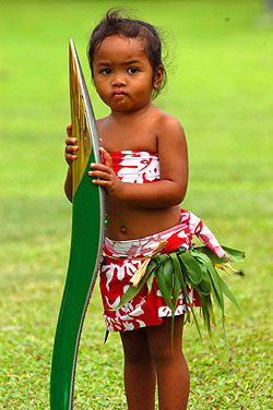 The relay continues in the Cook Islands. Dressed in island clothes, a local girl is bemused by the attention created by the baton's visit.