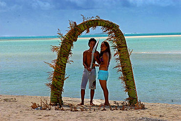 On Tapuae Tai (One Foot Island) a popular location for many tourists to marry, friends Royale and Teau stand with the Queen's Baton under a traditional wedding arch.